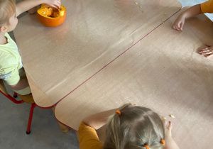 Dzieci przy stoliku wydrążają dynię