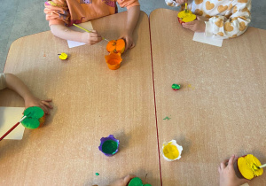 Dzieci przy stoliku malują farbami połówki jabłek