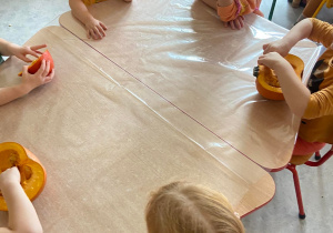 Dzieci przy stolikach oglądają przekrojoną dynię