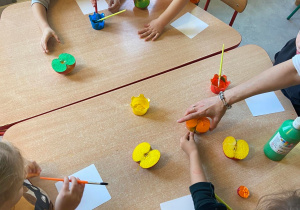 Dzieci przy stolikach odciskają połówki jabłka pomalowane farbą na kartki