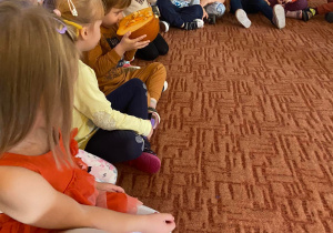 Dzieci na dywanie wąchają i oglądają przekrojoną dynię