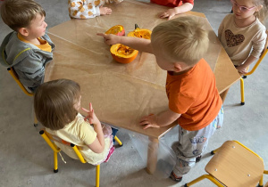 Dzieci przy stoliku przygotowują się do wydrążania dyni