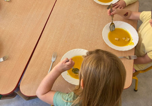 Dzieci przy stoliku jedzą zupę krem z dyni