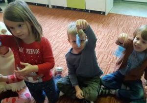 Dzieci siedzą na dywanie i pokazują odblaski w kształcie misia.