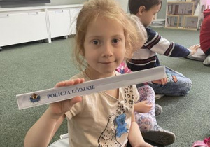 dziewczynka pokazuje opaskę odblaskową z napisem "Policja Łódzkie"