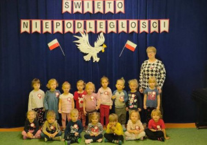 Dzieci z nauczycielką pozują do zdjęcia na tle dekoracji przygotowanej z okazji Narodowego Święta Niepodległości