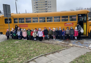 dzieci z nauczycielkami ustawione w rzędzie przed autobusem w amerykańskim stylu school bus