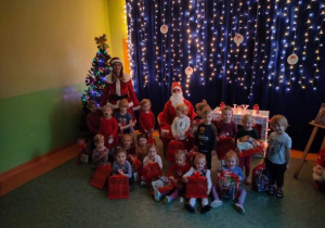 Dzieci obdarowane prezentami pozują do zdjęcia z Mikołajem i Mikołajką na tle świątecznej iluminacji