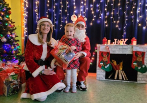 Dziewczynka pozuje do zdjęcia z Mikołajem i Mikołajką na tle świątecznej dekoracji