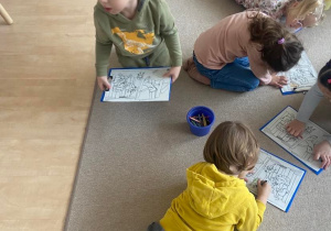 Dzieci na dywanie kolorują obrazki
