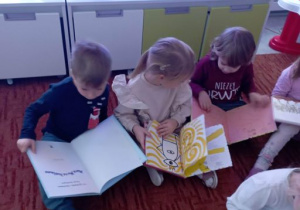 Dzieci oglądają książki siedząc na dywanie