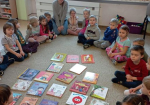 Dzieci z nauczycielką siedzą wokół rozłożonych na dywanie książek