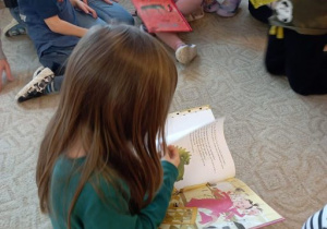 Dziewczynka ogląda książkę siedząc na dywanie