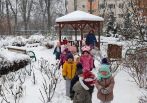 Dzieci z nauczycielką spacerują po zimowym ogrodzie przedszkolnym