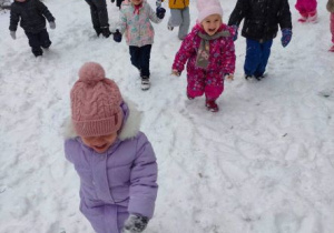 Roześmiane dzieci biegają po śniegu w ogrodzie przedszkolnym