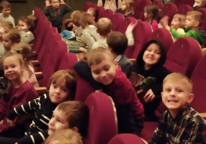 Widownia w teatrze. Dzieci siedzą w fotelach uśmiechają się.