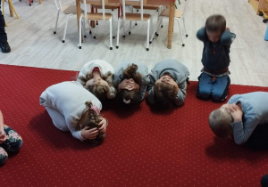 Sala przedszkolna. Dzieci siedzą na dywanie wykonują polecenia policjantki.