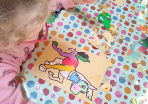 Dziewczynka sypie kolorowym piaskiem na obrazek przedstawiający jednorożca