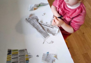 Dziewczynka koncentruje się na cięciu gazety na bardzo drobne elementy