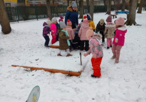 Dzieci z nauczycielką przyglądają się grządce pokrytej śniegiem
