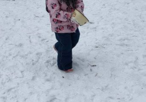 Dziewczynka idzie po śniegu z naczyniem z zimowej kuchni