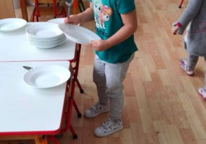 Dziewczynka bierze talerz i łyżkę do przygotowania nakrycia do obiadu