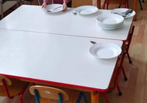 Dziewczynka kładzie talerz na zupę na stoliku przy swoim krzesełku