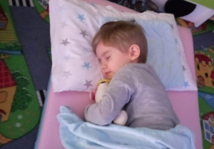 Chłopiec śpi na materacu przytulając maskotkę