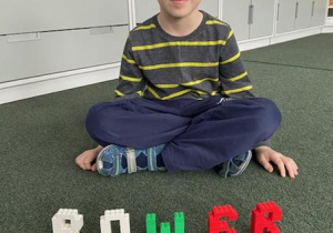 chłopiec prezentuje skonstruowane według wzoru litery z klocków ułożone w wyraz "rower"