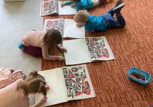Dzieci na dywanie rysują historyjki w książkach