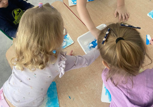 Dzieci przy stoliku malują farbą przy pomocy wacików