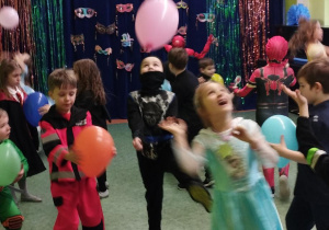 Sala gimnastyczna w przedszkolu. W tle dekoracja karnawałowa. Dzieci uczestniczą w zabawach z balonami.