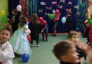 Sala gimnastyczna w przedszkolu. W tle dekoracja karnawałowa. Dzieci uczestniczą w zabawach z balonami.