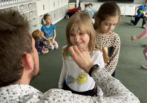 edukator maluje dziewczynce na twarzy kocie wąsy i uszy
