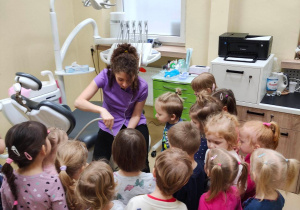 Dzieci stoją wokół Pani dentystki demonstrującej działanie jednego z narzędzi stomatologicznych