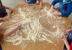 Dzieci rysują mąką rozsypaną na stoliku