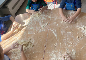 Dzieci przy stoliku wyrabiają ciasto z mąki i wody