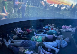 dzieci leżą w ciemnym namiocie Mobilnego Planetarium i poznają Układ Słoneczny