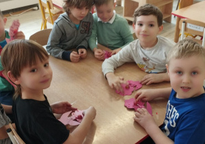 Sala przedszkolna. Dzieci siedzą przy stoliku i wykonują pracę plastyczną
