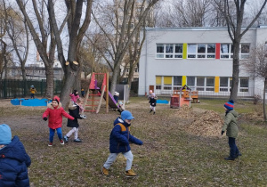 Ogród przedszkolny. Dzieci biegają po ogrodzie. Szukają oznak wiosny.