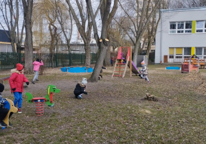 Ogród przedszkolny. Dzieci biegają po ogrodzie. Szukają oznak wiosny.