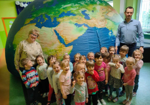 Dzieci z nauczycielką i edukatorem pozują do zdjęcia przed kopułą mobilnego planetarium przypominającą kulę ziemską