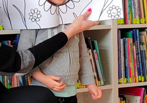 Dziewczynka pozuje do zdjęcia wypełniając swoją głową dziurę w ilustracji przedstawiającej kwiatka