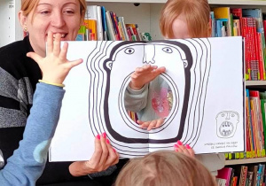 Dziewczynka układa ręce w dziurze książki tak, by imitowały zęby w otwartej buzi postaci z książki