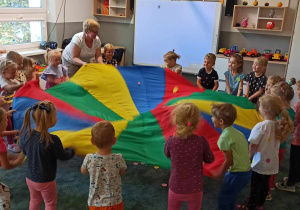 Dzieci z nauczycielką tworzą deszcz z kropek podczas zabawy chustą animacyjną