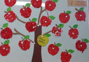 Prezentacja pracy plastycznej na tablicy. Kształt jabłka wyklejany kawałkami czerwonej bibuły.