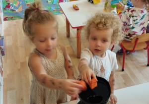 Sala przedszkolna. Dwie dziewczynki wrzucają marchewkę do wyciskarki.