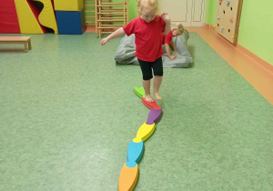 Dziewczynka próbuje zachować równowagę podczas przechodzenia przez kładkę gimnastyczną