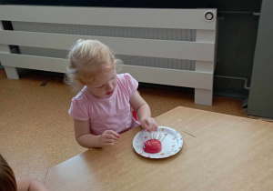 Dziewczynka dekoruje wykałaczkami jeżyka z jabłka