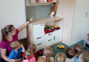 Dzieci z panią obserwują kotka próbującego wspiąć się na szafę